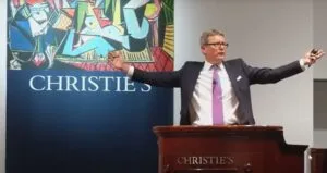 Auctioneer presenting at Christie's with colorful backdrop.