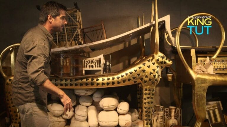 Man examining Tutankhamun's replica artifacts in museum display.