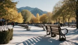 Snowy park with benches and mountains in background.